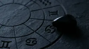 Simbolo zodiacale del Cancro inciso su una superficie scura con una pietra nera appoggiata sopra