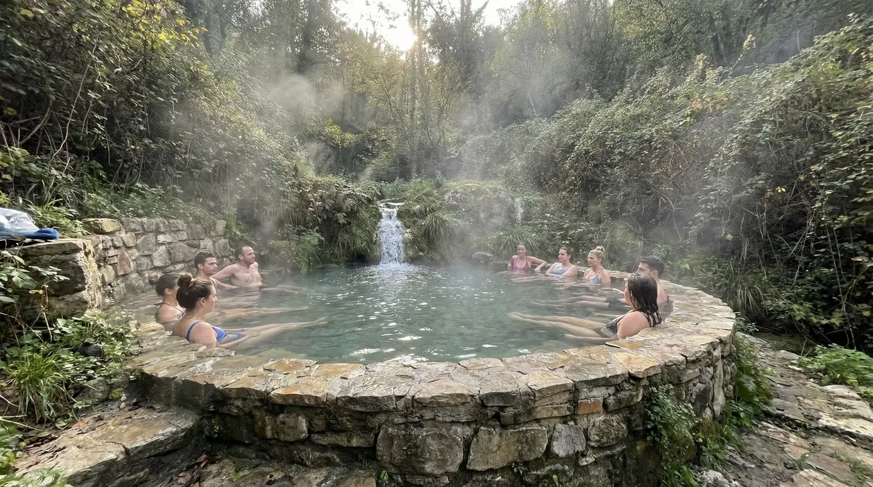 Persone immerse in una piscina termale naturale circondata dalla natura