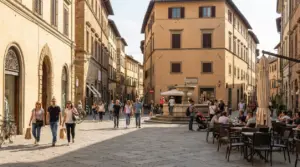 Persone che passeggiano in una piazza pedonale con caffè all’aperto e una fontana centrale